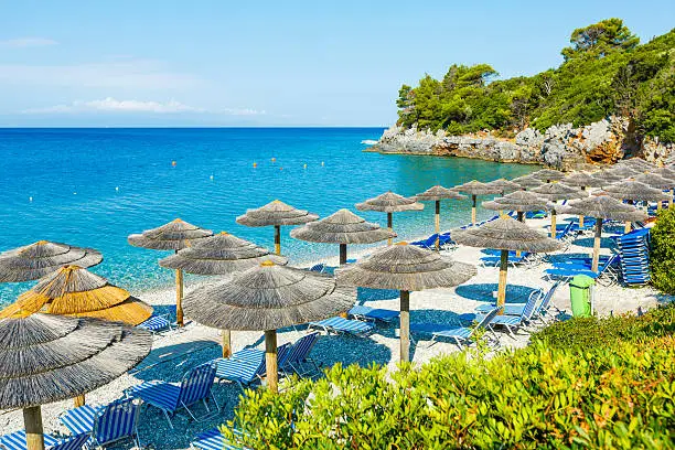 Lounge chairs and umbrella at private beach near town Panormos village, Skopelos island, Greece. Property released.