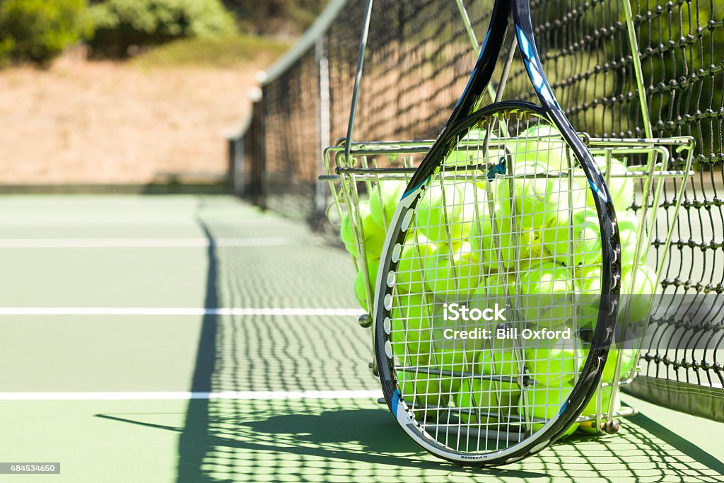 Tennis balls and racquet on court Tennis balls and racquet on court showing net and lines of court with basket of balls Tennis Stock Photo