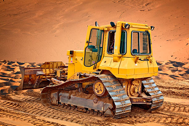 Yellow bulldozer leveling sand dunes in the desert for the construction of a new road