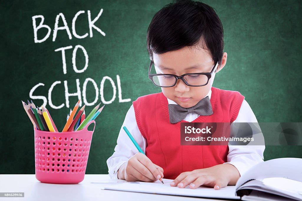 Child back to school and drawing in the class Cute little boy wearing uniform and back to school, drawing on the book in the classroom Child Stock Photo