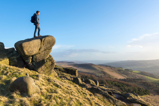 Young male hiker stood on rocky outcrop, Stanage Edge, Peak District.