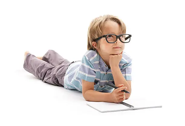 Thinking or day dreaming boy doing homework with glasses, notepad and pencil isolated on white background