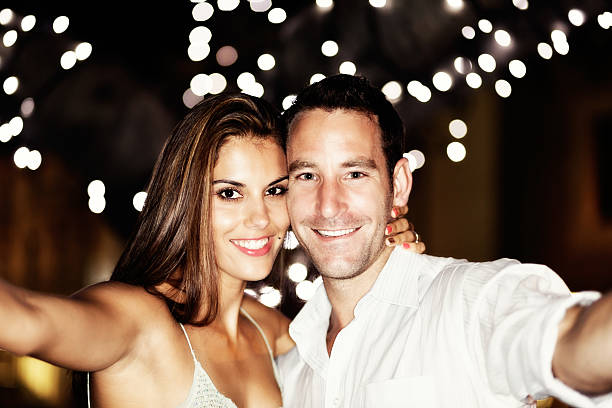 istock Under twinkling lights, a smiling couple take a cellphone selfie 484553878