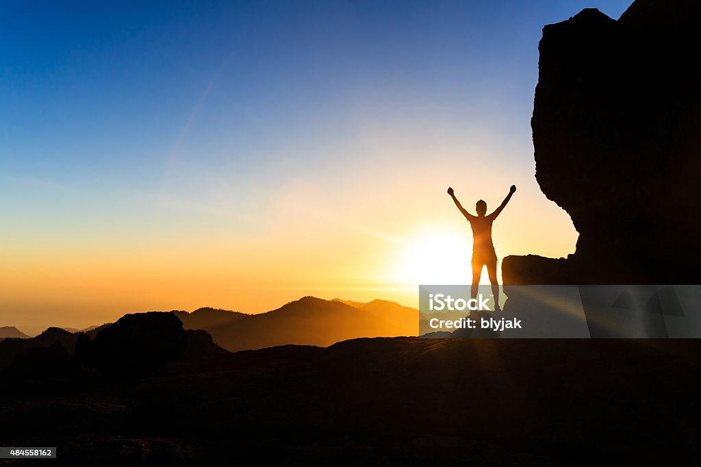 Woman climber success silhouette in mountains, ocean and sunset Woman successful hiking climbing silhouette in mountains, motivation and inspiration in beautiful sunset and ocean. Female hiker with arms up outstretched on mountain top looking at beautiful night sunset inspirational landscape. Conquering Adversity Stock Photo