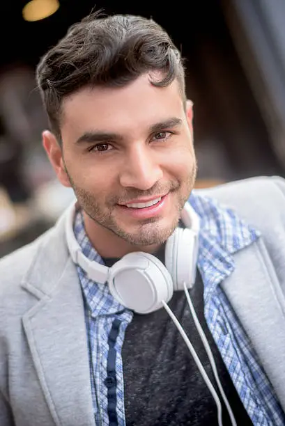 Portrait of a casual Latin American man with headphones listening to music and looking at camera smiling