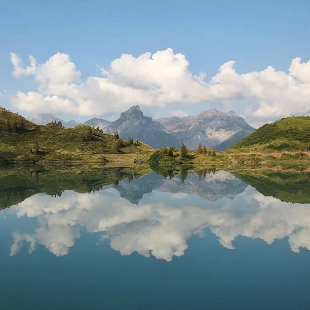 Mountains, trees and summer cloud mirroring in lake Trubsee, Titlis region.