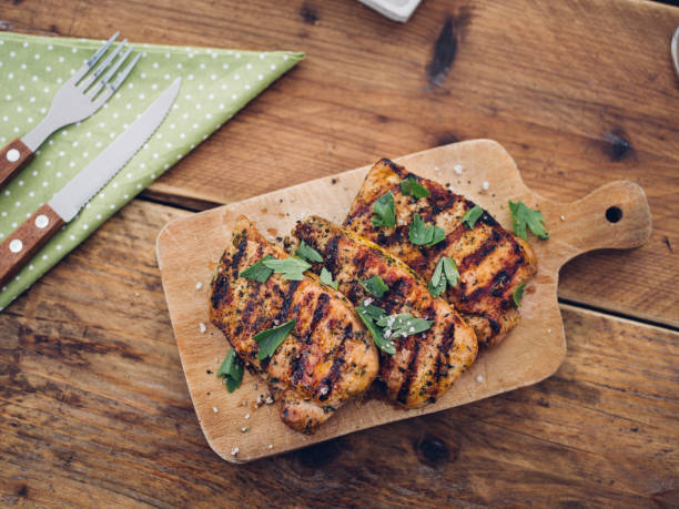 Overhead shot of three healthy grilled pork fillets looking delicious and sprinkled with fresh herbs on a wooden board