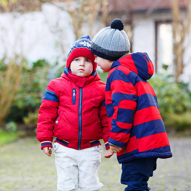 Two little sibling boys in red jackets hugging