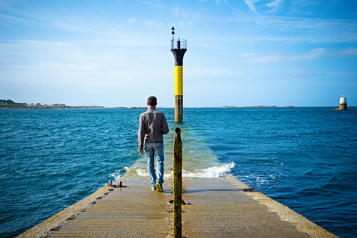 Man walking to a lighthouse during low tide in the Atlantic Ocean. Britain, France 