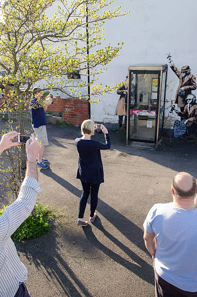 Possible Banksy artwork, Cheltenham Cheltenham, United kingdom - April 13, 2014: Members of the public taking photos of a possible Banksy graffiti artwork that appeared overnight on the side of a house in Cheltenham. It depicts three government agents monitoring phone conversations from a phone box.  banksy stock pictures, royalty-free photos & images