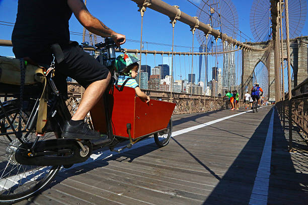 New York, USA - August 09, 2015: a man cycles with his child on Brooklyn Bridge. Other bikers and pedestrians are visible on the bridge.