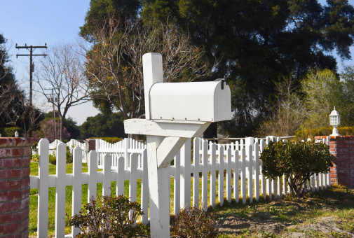 Single mailbox sits in front of a white picket fence.