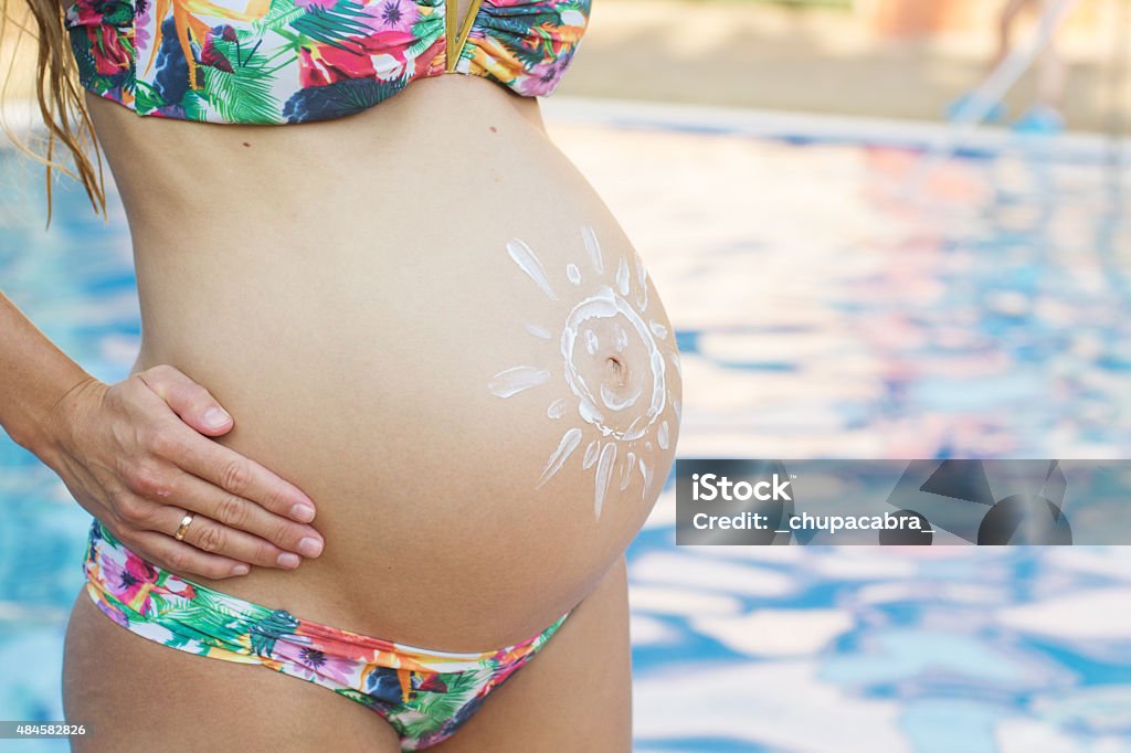Sun shape picture on pregnant belly Closeup picture of belly of pregnant girl with sun picture over swimming pool with blue water 2015 Stock Photo