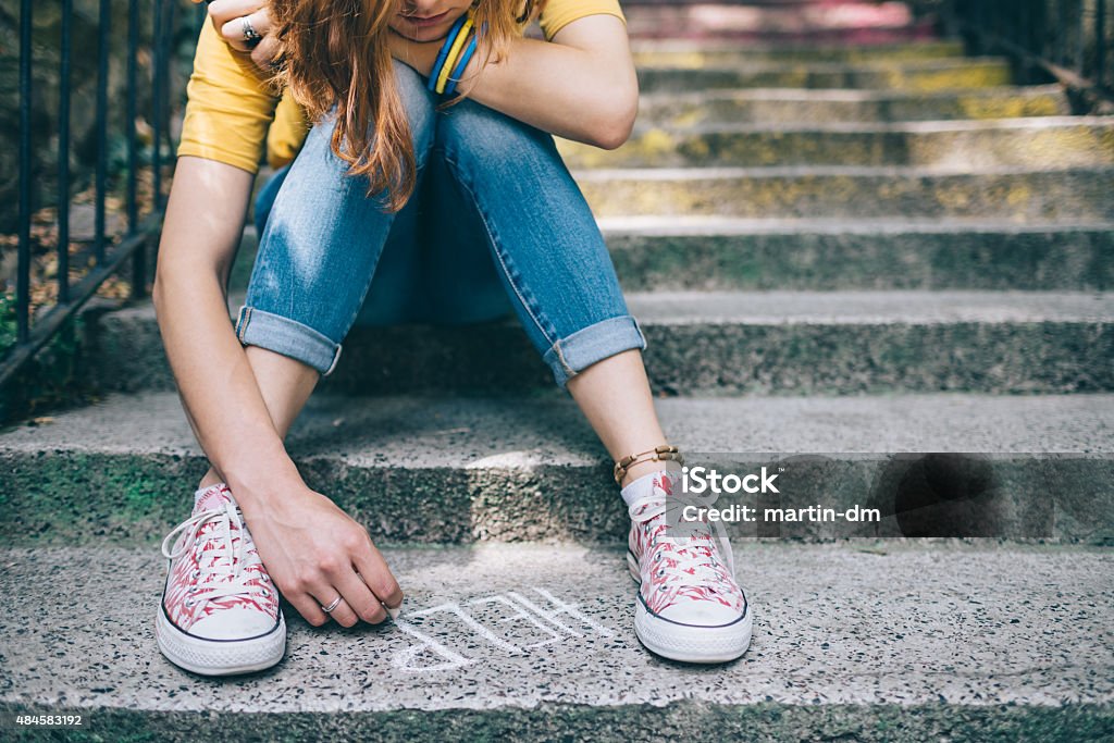 Unahppy girl writes help on the ground Teenage grl sitting on a staircase outside feeling depressed Teenager Stock Photo