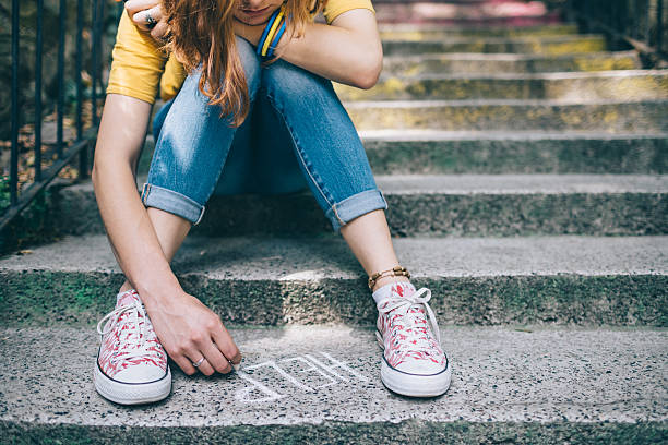 Unahppy girl writes help on the ground Teenage grl sitting on a staircase outside feeling depressed gloomy mood stock pictures, royalty-free photos & images