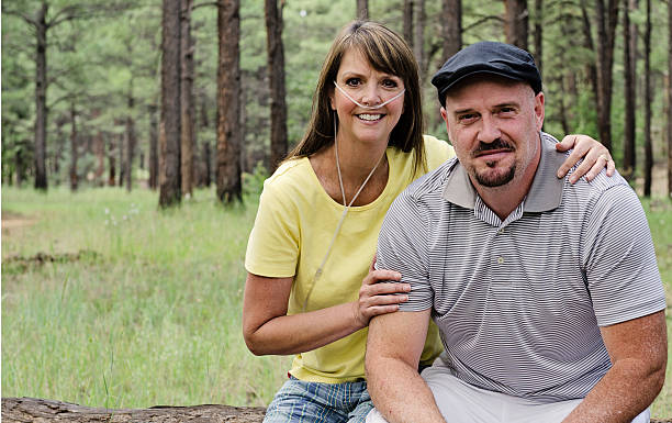 Mid Age Couple Women Wearing Oxygen Portrait of a happy couple enjoying the out of doors with the woman wearing a therapeutic oxygen canula. medical oxygen equipment stock pictures, royalty-free photos & images