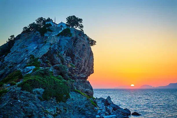Rock with famous church Agios Ioannis Kastri on Skopelos island, Greece at sunrise, where scenes of Mamma Mia movie were filmed. Sun raises above Alonissos island.