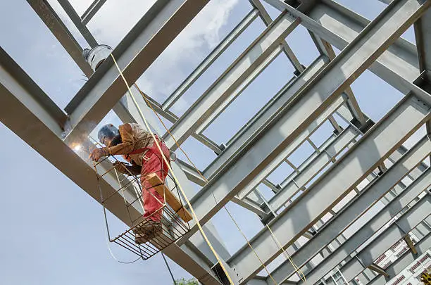 Welder soldering metal girders in a structure high above