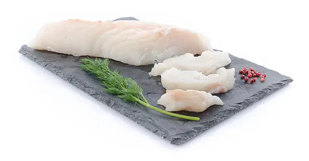 Fresh raw cod fillet on a slate plate, isolated on white