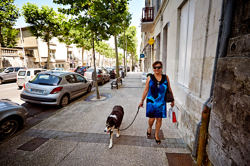 Saintes, France - June 20, 2015: Mature hispanic woman walking dog on French street in the town of Saintes