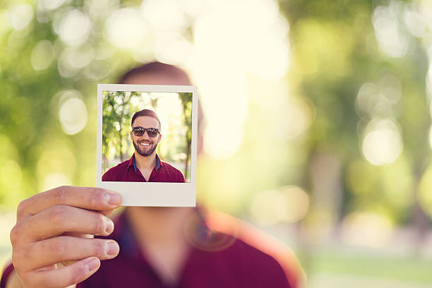 Man holding instant selfie Young man in the park showing a self polaroid portrait in front of photos stock pictures, royalty-free photos & images