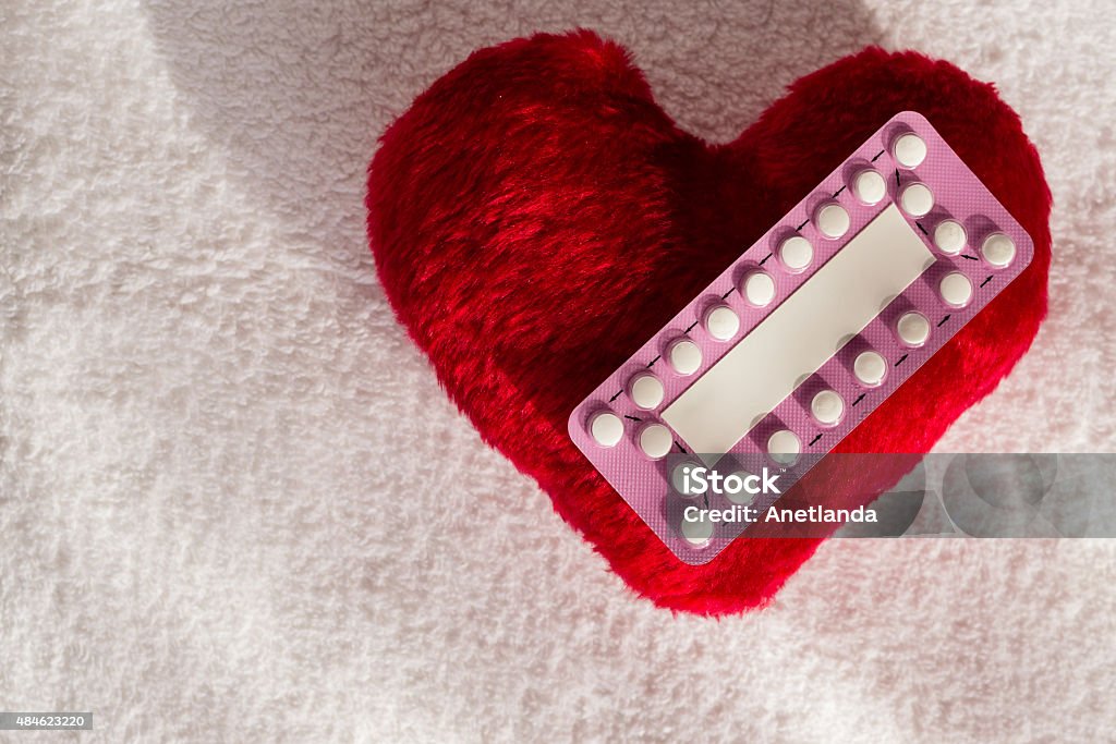 Oral contraceptive pills on red heart Medicine contraception love and birth control. Oral contraceptive pills on red heart shaped little pillow 2015 Stock Photo