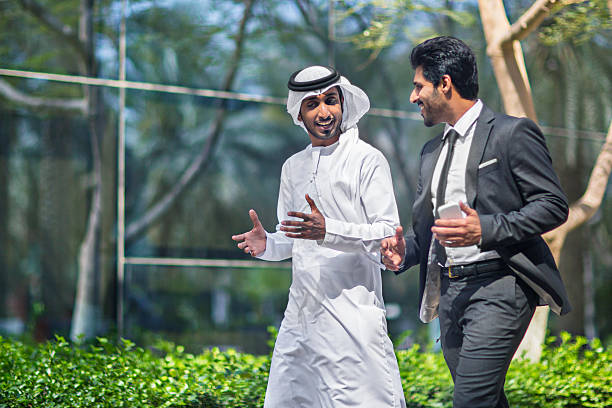 Middle Eastern businessmen talking in the street Middle Eastern businessmen talking in the street about business, one is wearing the typical dishdasha and the other a suit. west asia stock pictures, royalty-free photos & images
