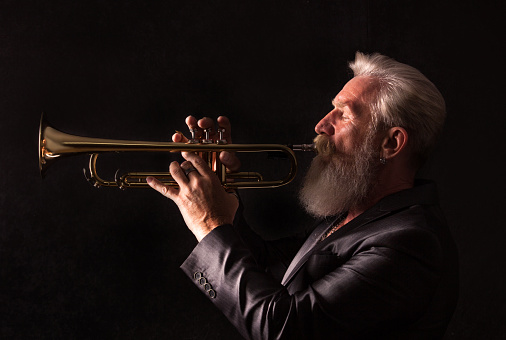 PIcture of a white haired trumpet player with a long white beard. Profile picture with side light.