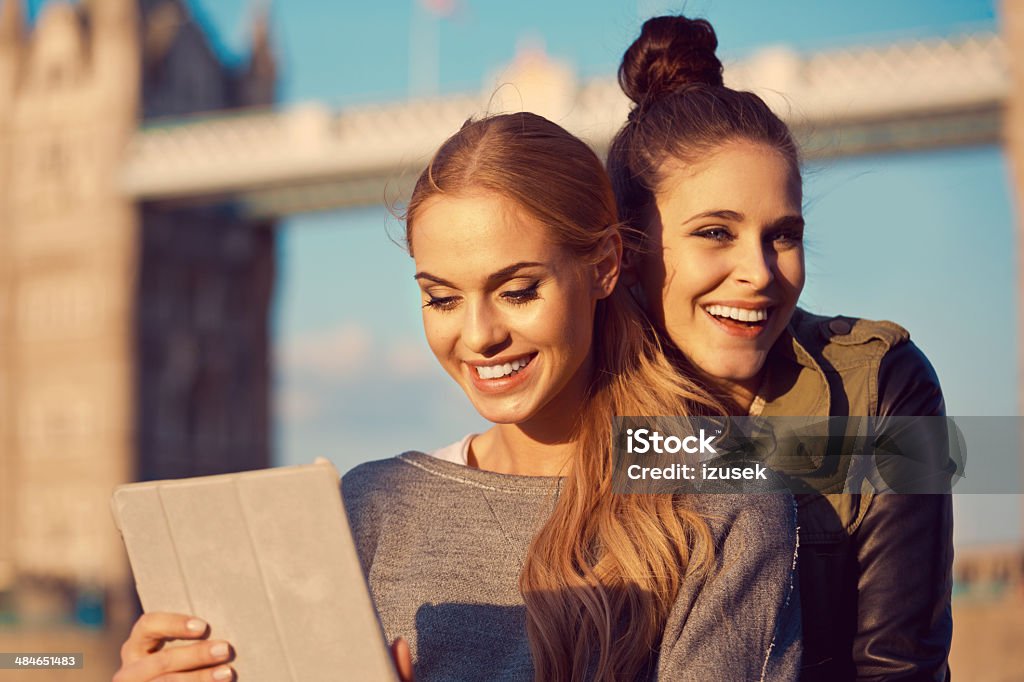 Friends in London Outdoor portrait of two happy young women using a digital tablet with Tower Brigde in the background. 20-24 Years Stock Photo