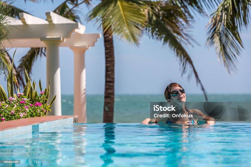 Woman Relaxing Inside Infinity Pool At Tropical Resort Woman Relaxing Inside Infinity Pool At Tropical Resort in Vietnam. There is some palm trees and the sea in the background o this beautiful sunny day. Active Lifestyle Stock Photo