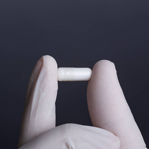 istock Hand in white latex glove holding a capsule 484654517
