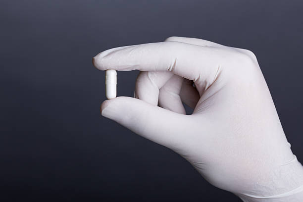 la main dans un gant en latex blanc tenant une capsule - surgical glove human hand holding capsule photos et images de collection
