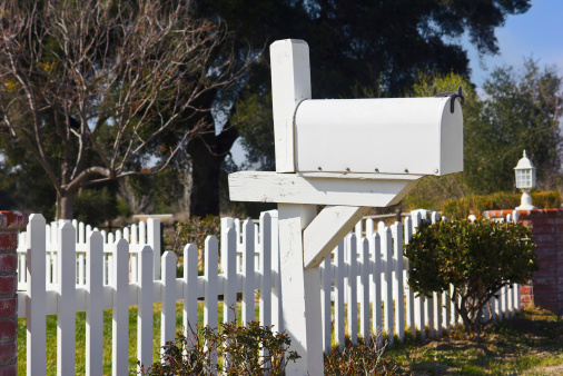 Mailbox sits in the front yard next to a white picket fence.