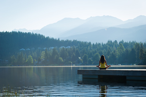 Female meditating doing sukhasana or Easy Pose during a yoga working at a pristine mountain lake