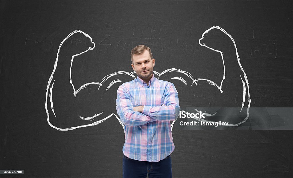 Young handsome man in casual shirt with drawn powerful hands Young handsome man in casual shirt with drawn powerful hands. Black chalkboard background. Flexing Muscles Stock Photo