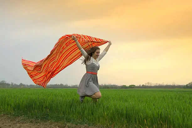 Smiling woman running with veil at the sunset