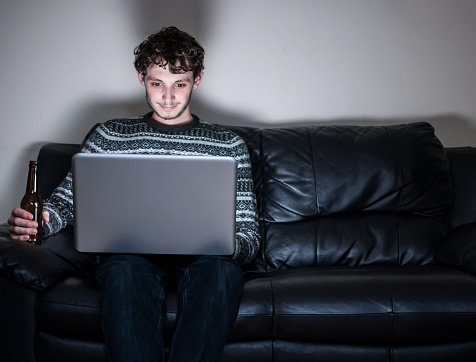Young Man on Black Sofa with Laptop and beer