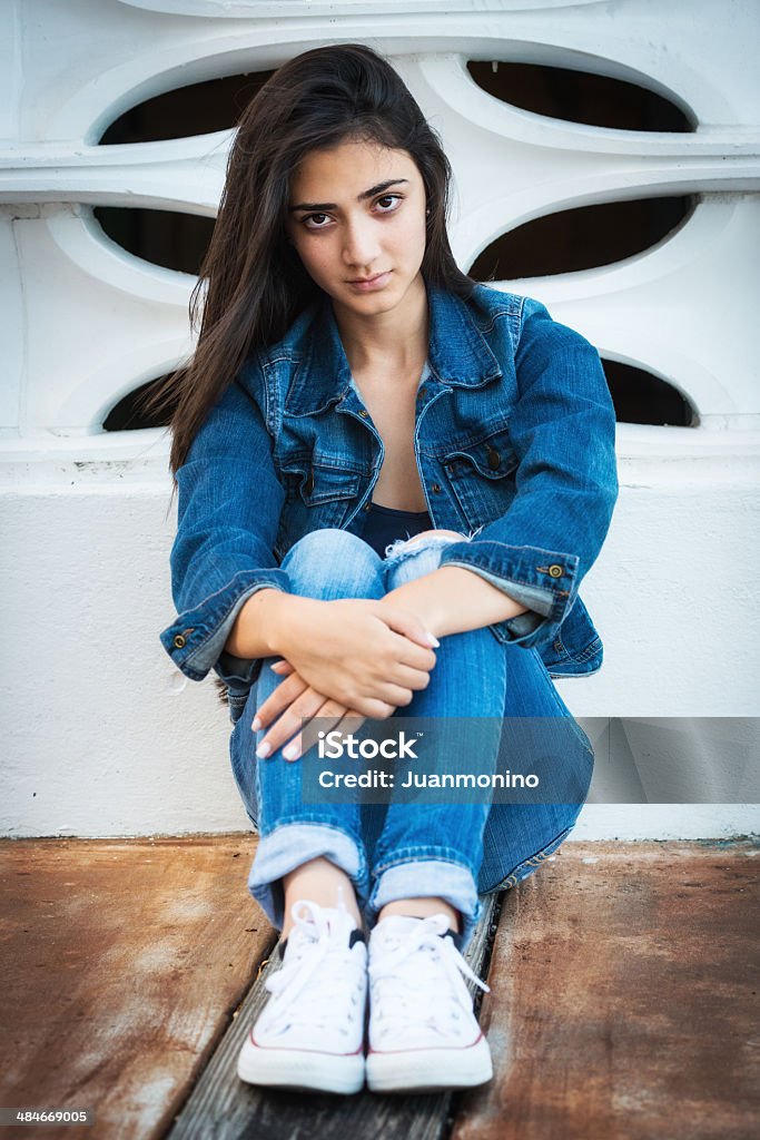 Serious teenage girl Serious Hispanic teenage girl sitting on the floor 16-17 Years Stock Photo