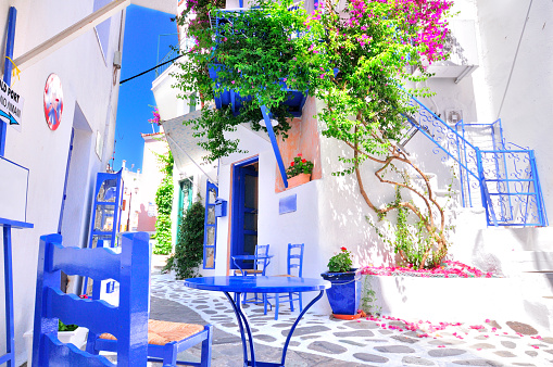 Traditional greek architecture in a narrow alley in Skiathos town, Sporades archipelago, Greece with cobblestone pathways, blue painted windows, door and furniture, whitewashed walls and beautiful bougainvillea in full bloom. All signs are edited except the one that says \