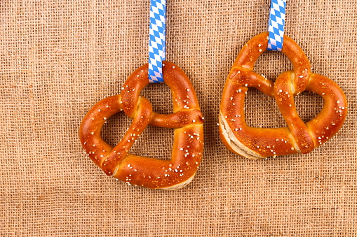 Two pretzel in heart shape on jute background, top view