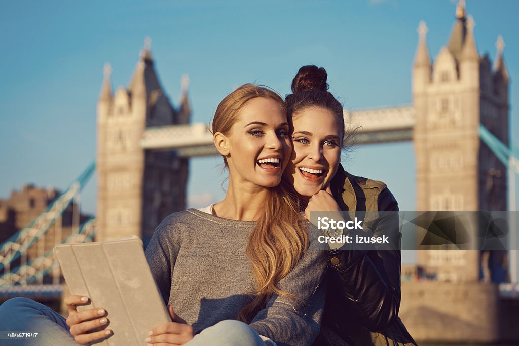 Friends in London Outdoor portrait of two happy young women taking a self picture using a digital tablet with Tower Brigde in the background. 20-24 Years Stock Photo