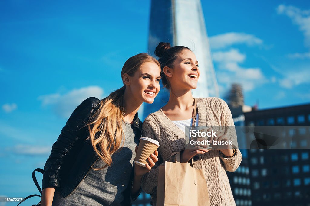 London tourists Outdoor portrait of two young happy women holding take away coffee in hands, looking away, with The Shard Tower in the background. Coffee - Drink Stock Photo