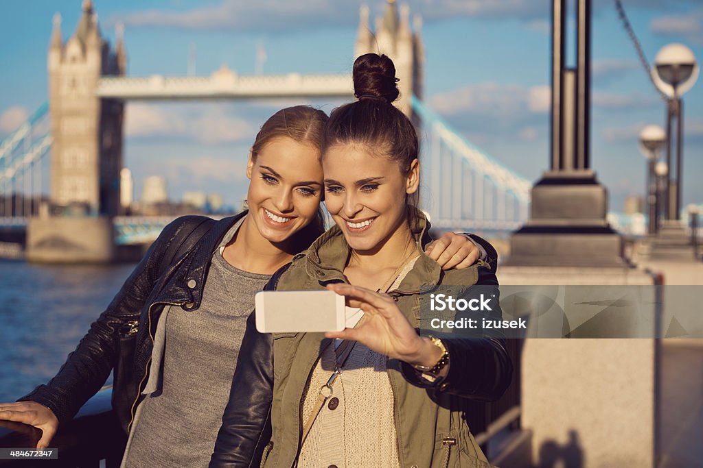 London tourists Outdoor portrait of two young women taking a self picutre using smart phone with Tower Brigde in the background. 20-24 Years Stock Photo