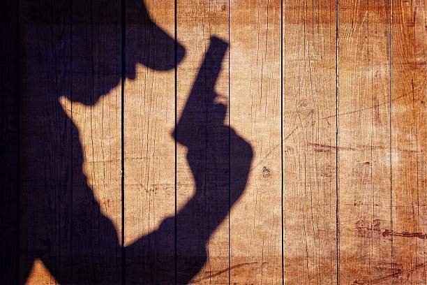 istock Man with a gun in shadow on a wooden background 484675253