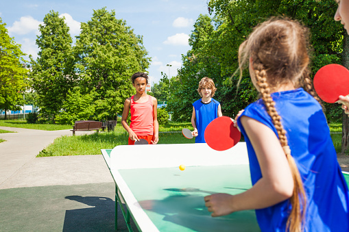 Four international friends playing table tennis  outside during summer sunny day
