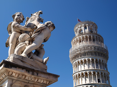 Cupid statue with the leaning tower of Pisa in the background during summer