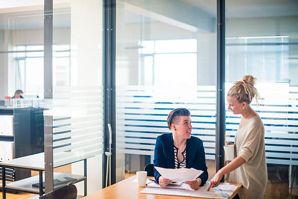 istock Businesswomen communicating over blueprint at conference table 484680134