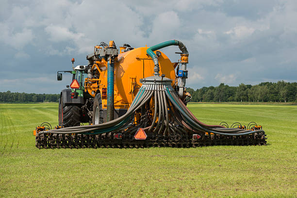 Injecting liquide manure with tractor Agriculture, injecting of liquid manure with green tractor and yellow vulture spreader trailer. animal dung stock pictures, royalty-free photos & images