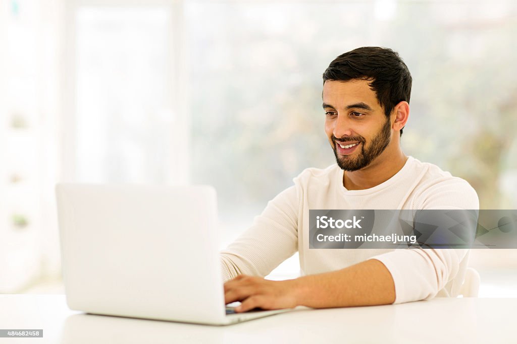 young indian man using laptop smiling young indian man using laptop at home 2015 Stock Photo