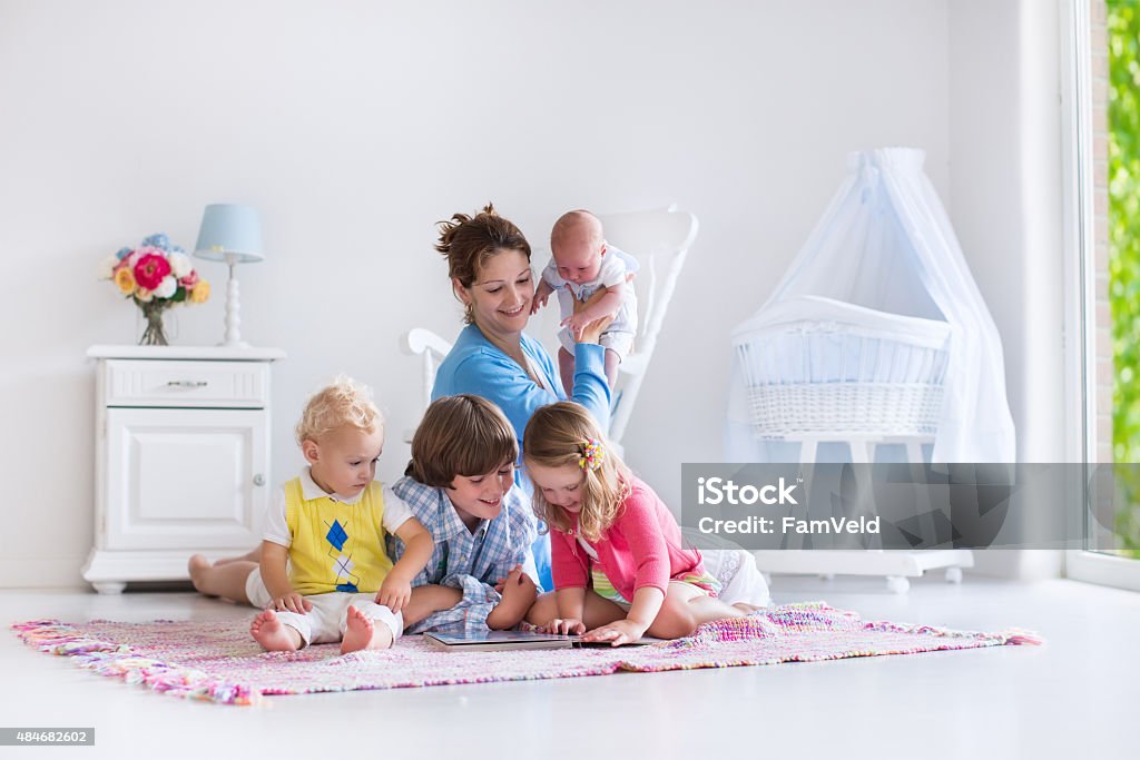 Mother and kids playing in bedroom Mother and children play indoors. Family with kids in a white bedroom. Mom with baby, boy and girl playing and reading books at home. Beautiful nursery for baby and toddler. Room for preschool child. Newborn Stock Photo